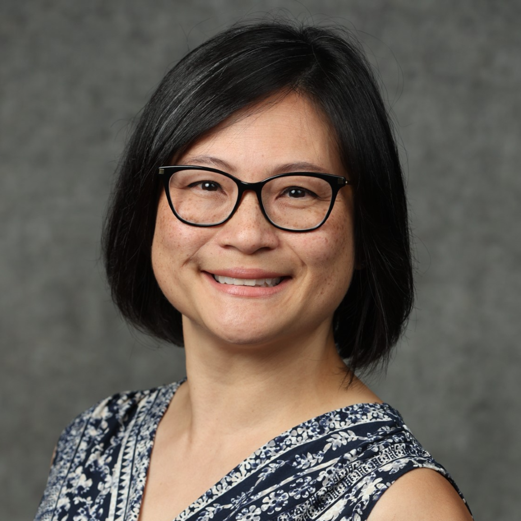 Woman with short black hair, smiling, wearing black glasses